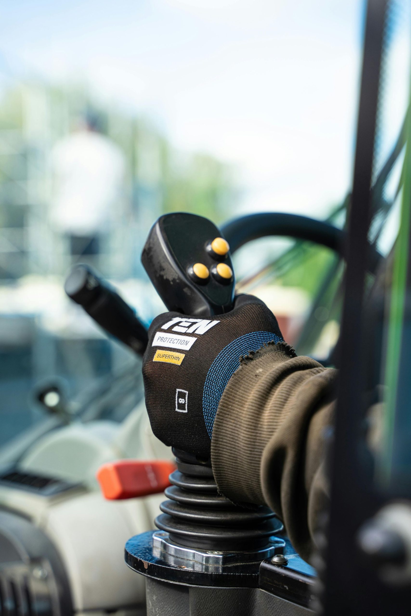 Gloved hand operating a joystick inside an equipment cab.